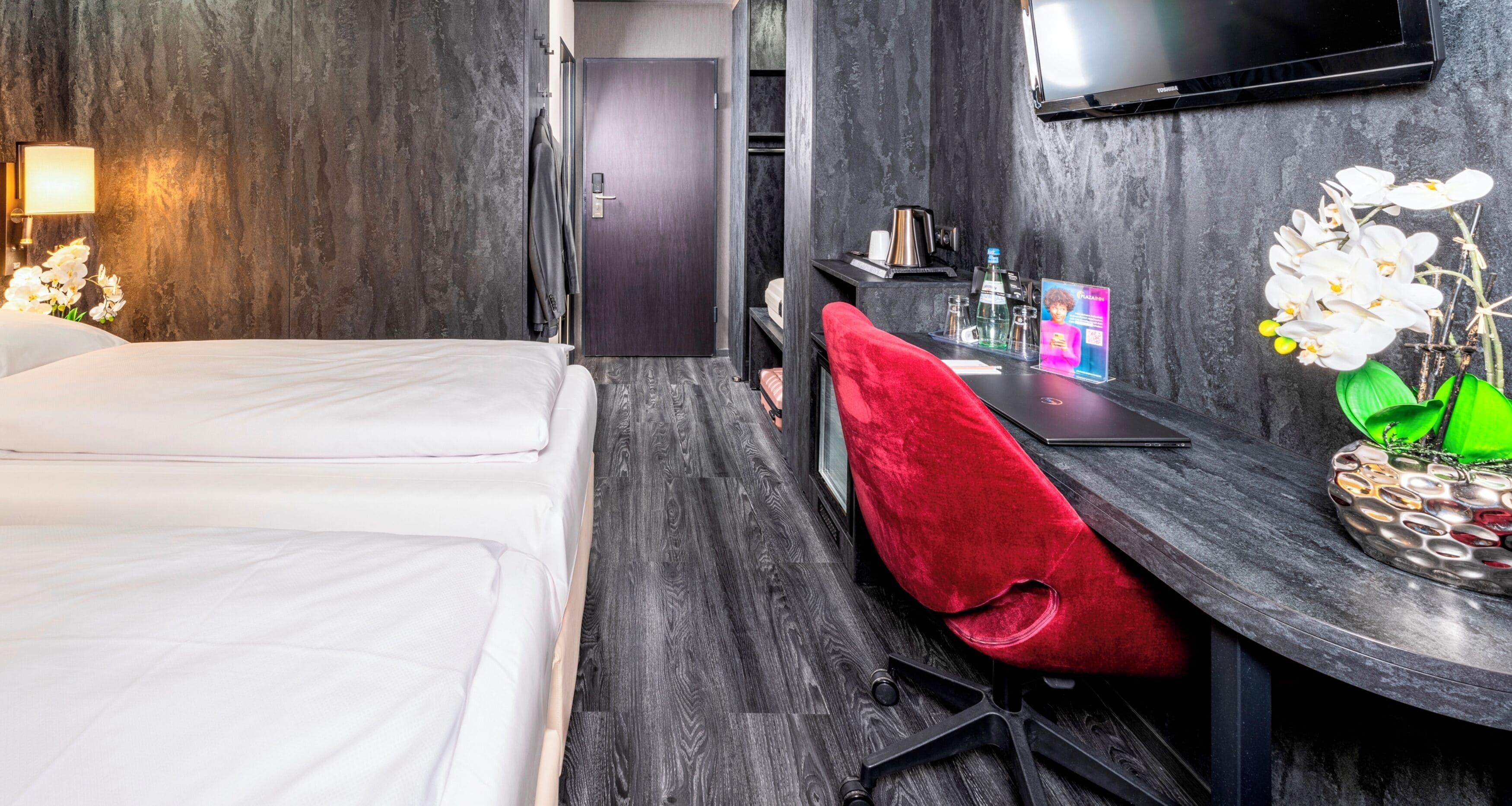 Een hotelkamer met een bed, een bureau met een stoel, een televisie en een tafeltje met een bloevas.