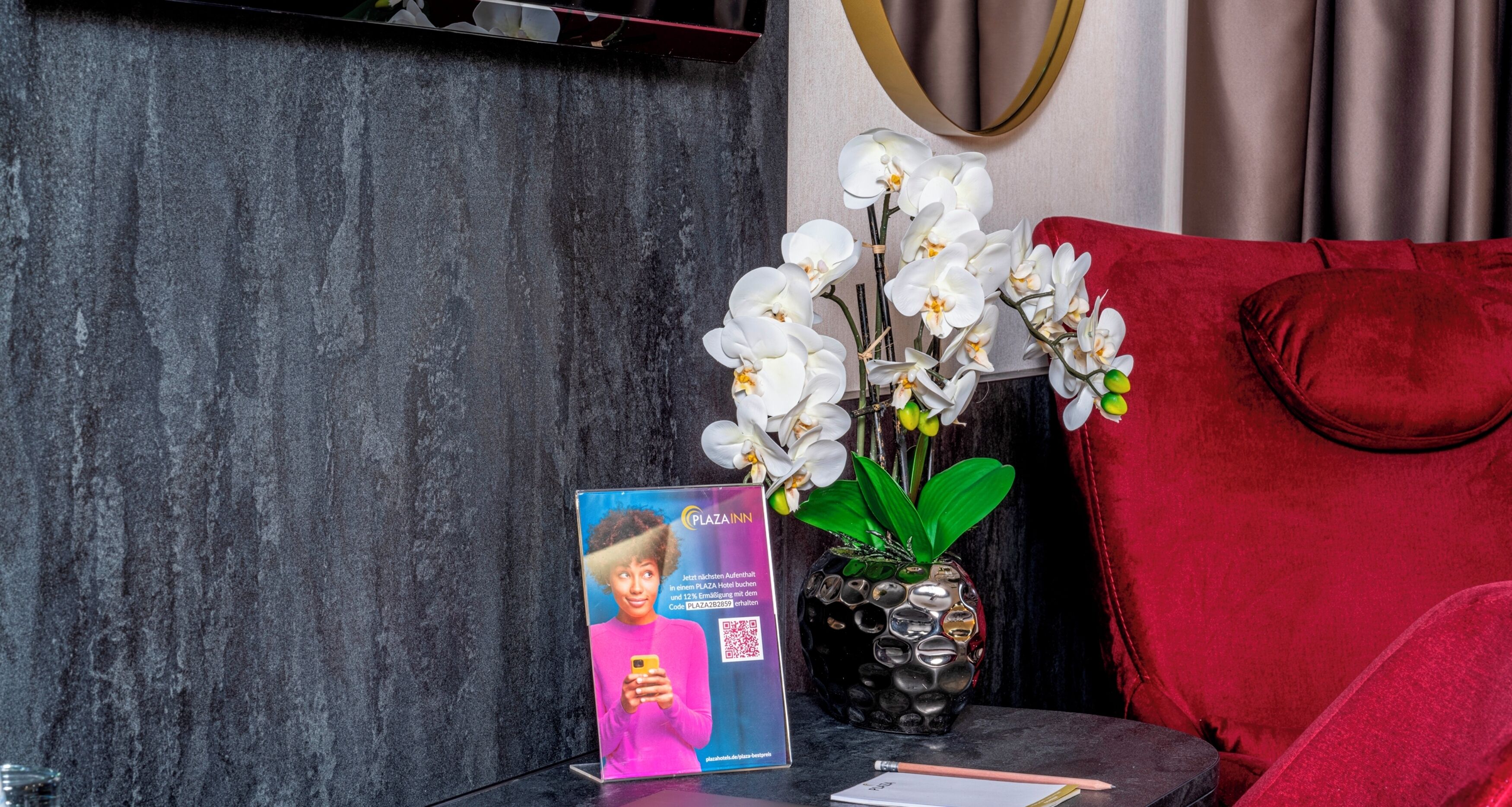 A promotional display with a QR code, a brochure, and a vase with white orchids on a table.