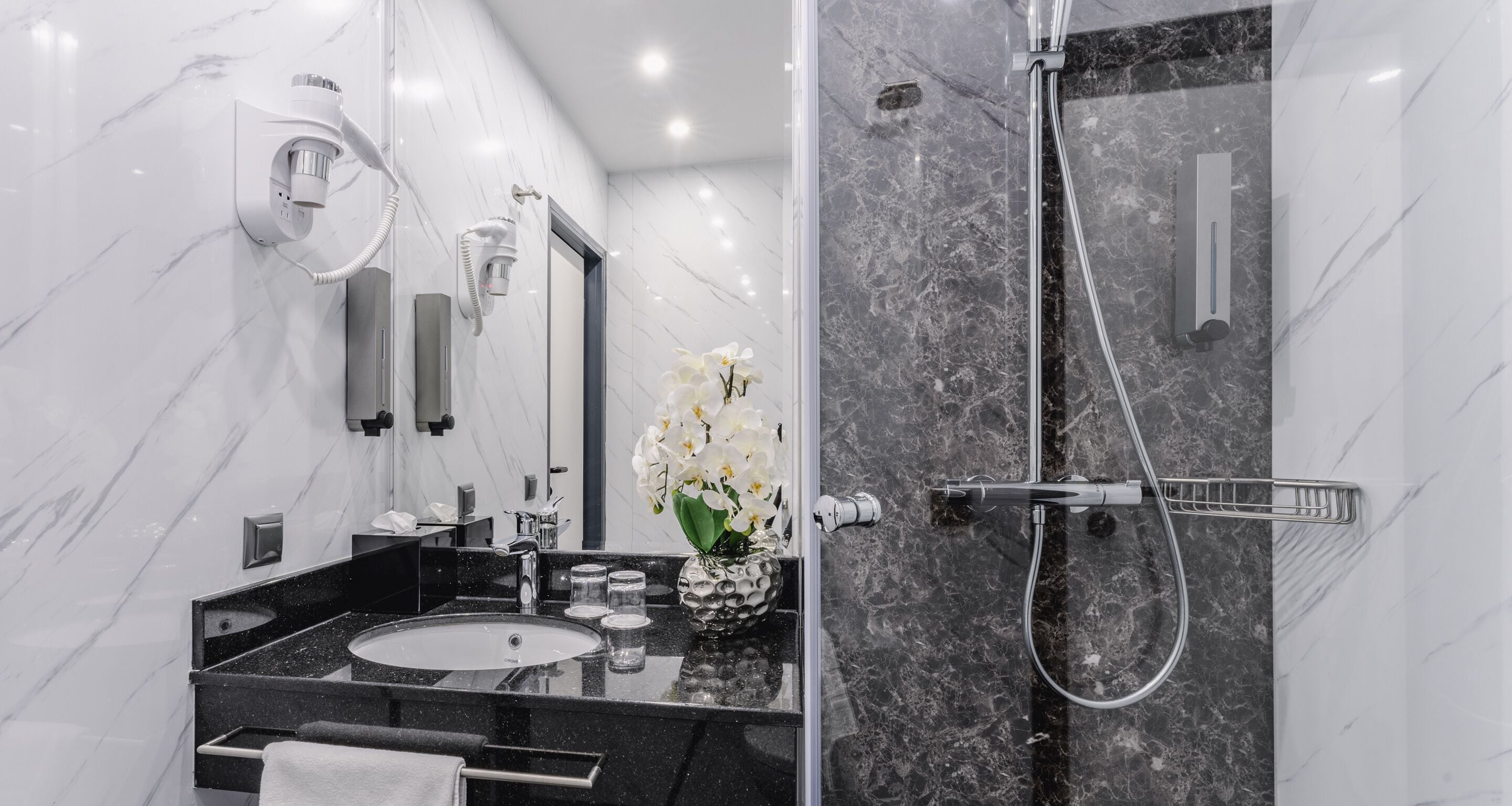 Un baño moderno con lavabo de mármol, cabezal de ducha de mano y espejo con luz integrada.