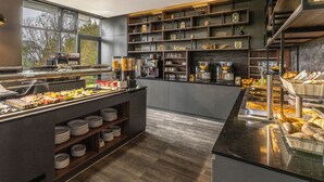A buffet area with various food items, a coffee station, and a display of bread and pastries. - PLAZA INN Mühldorf am Inn (Muhldorf am Inn)