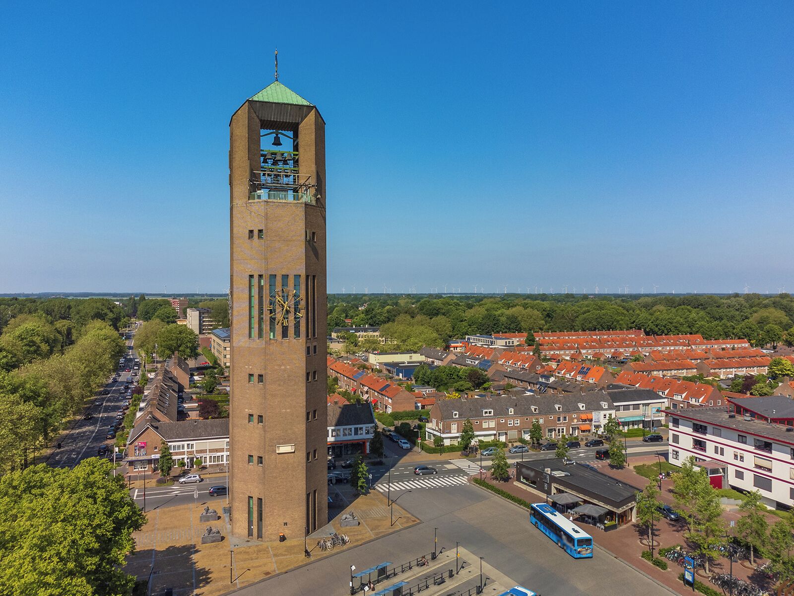 Een hoge bakstenen toren met een klok, omringd door woongebouwen en een heldere lucht.
