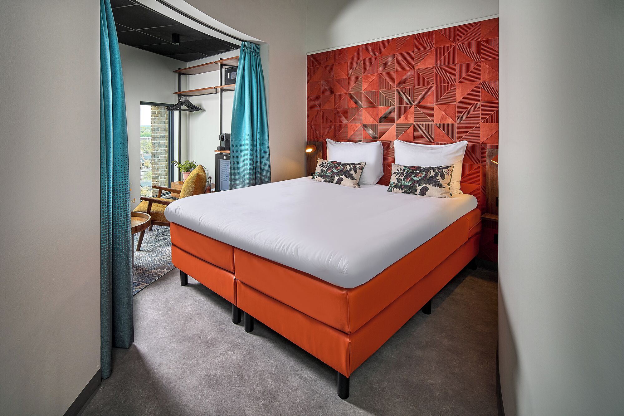 Una habitación de hotel moderna con una cama grande, un cabecero rojo estampado y vistas al exterior.