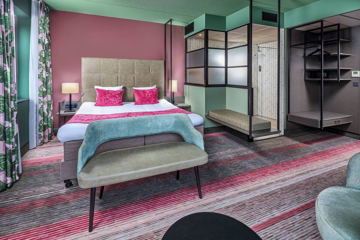 A hotel room with a bed, bedside tables, a bench, a wardrobe, and a mirror.