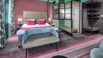 Een hotelkamer met een bed, nachtkastjes, een bankje, een garderobe en een spiegel.