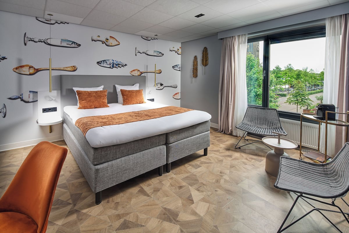 A hotel room with a bed, a chair, a table, and a view of the outdoors.