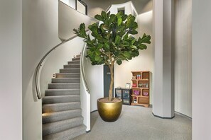 A staircase with a large potted tree, a bookshelf with books and decorative items, and a number '108' on the wall. - Hotel Restaurant Grandcafé 't Voorhuys (Emmeloord)