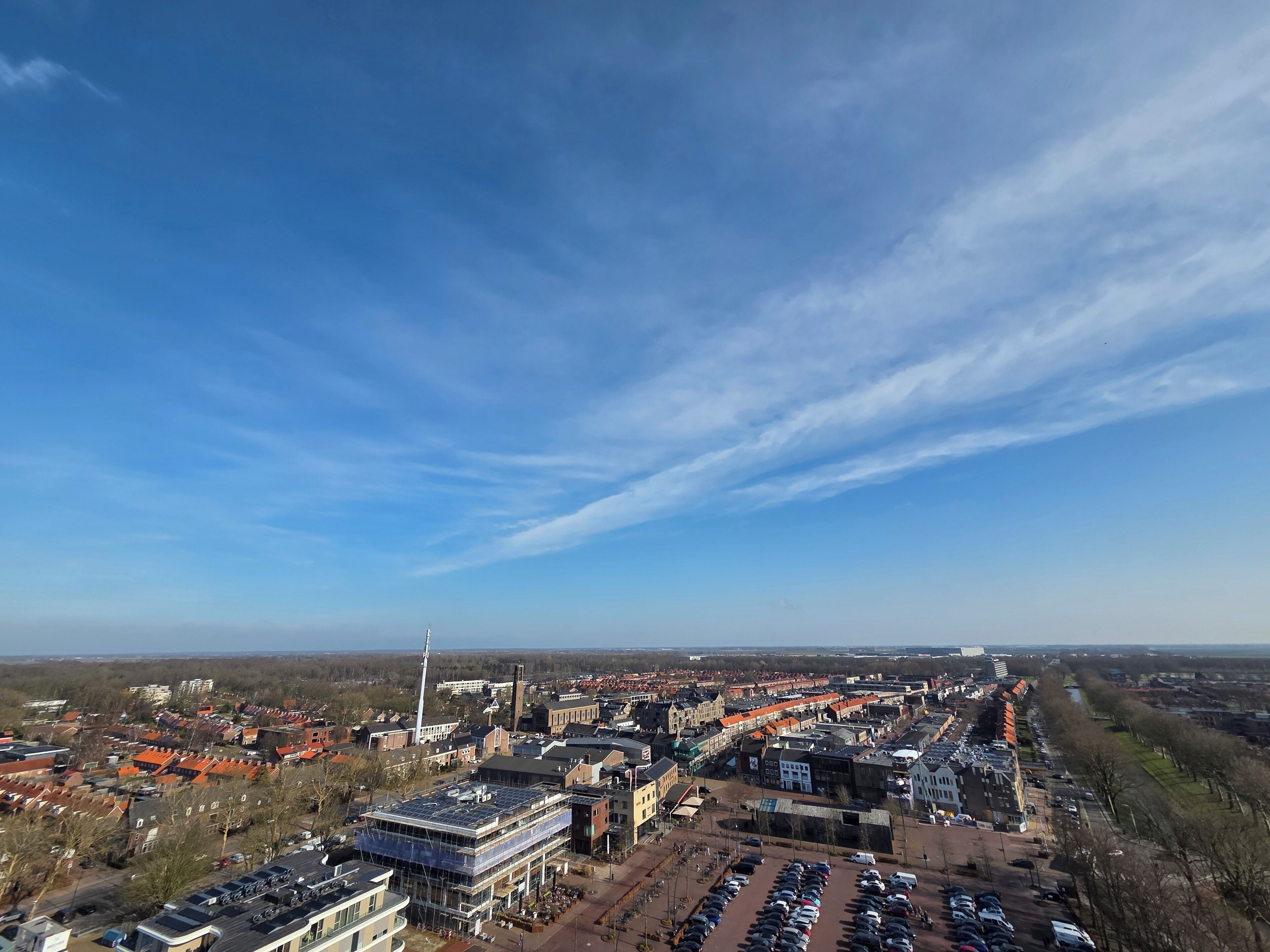 Une vue aérienne d’une ville où se côtoient des immeubles résidentiels et commerciaux, un vaste parking et une tour imposante.