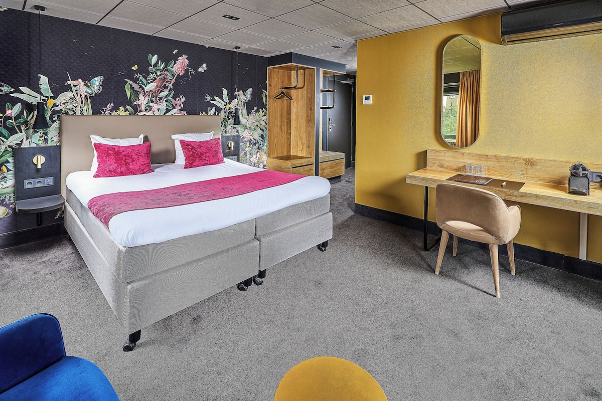 A hotel room with a bed, a desk, a chair, and a mirror.
