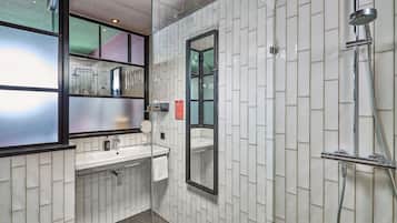 A modern bathroom with white tiled walls, a glass shower enclosure, a sink with a mirror, and a towel hanging on the wall.