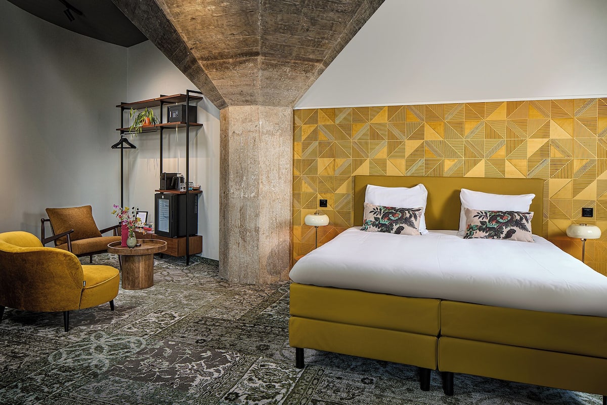 A hotel room with a bed, a sofa, a coffee table, and a floor lamp.