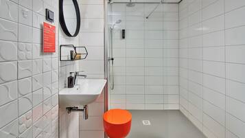 A modern bathroom with a white tiled wall, a white sink, a mirror, and a shower area.