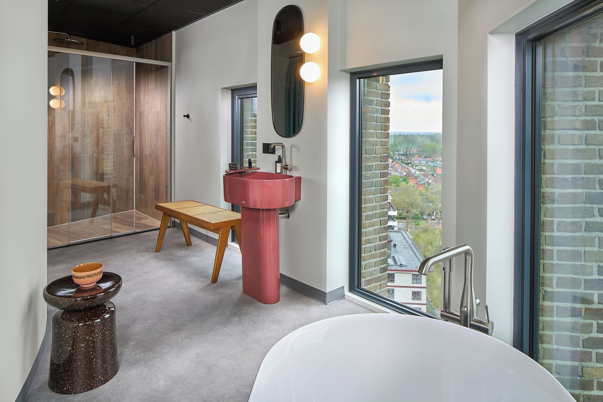 Een moderne badkamer met een groot raam, een rode wastafel en een houten bankje.