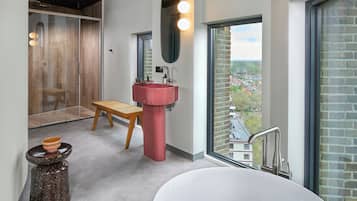 Een moderne badkamer met een groot raam, een rode wastafel en een houten bankje.