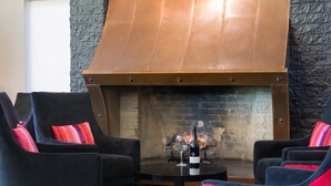 A cozy seating area with a fireplace, two armchairs with colorful cushions, and a table with a bottle and glass. - Croydon Lodge Hotel (Croydon)