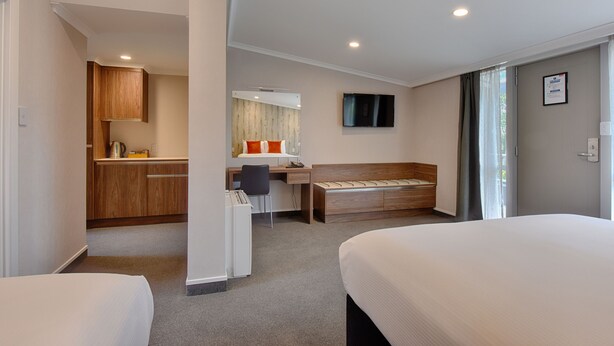 A hotel room with two beds, a desk, a chair, a TV, and a kitchenette. - Croydon Lodge Hotel (Croydon)