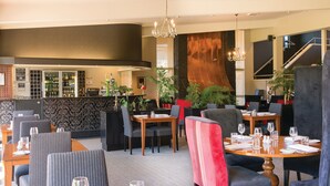 A restaurant with multiple dining tables and chairs, a bar area with a variety of bottles, and a staircase leading to an upper level. - Croydon Lodge Hotel (Croydon)