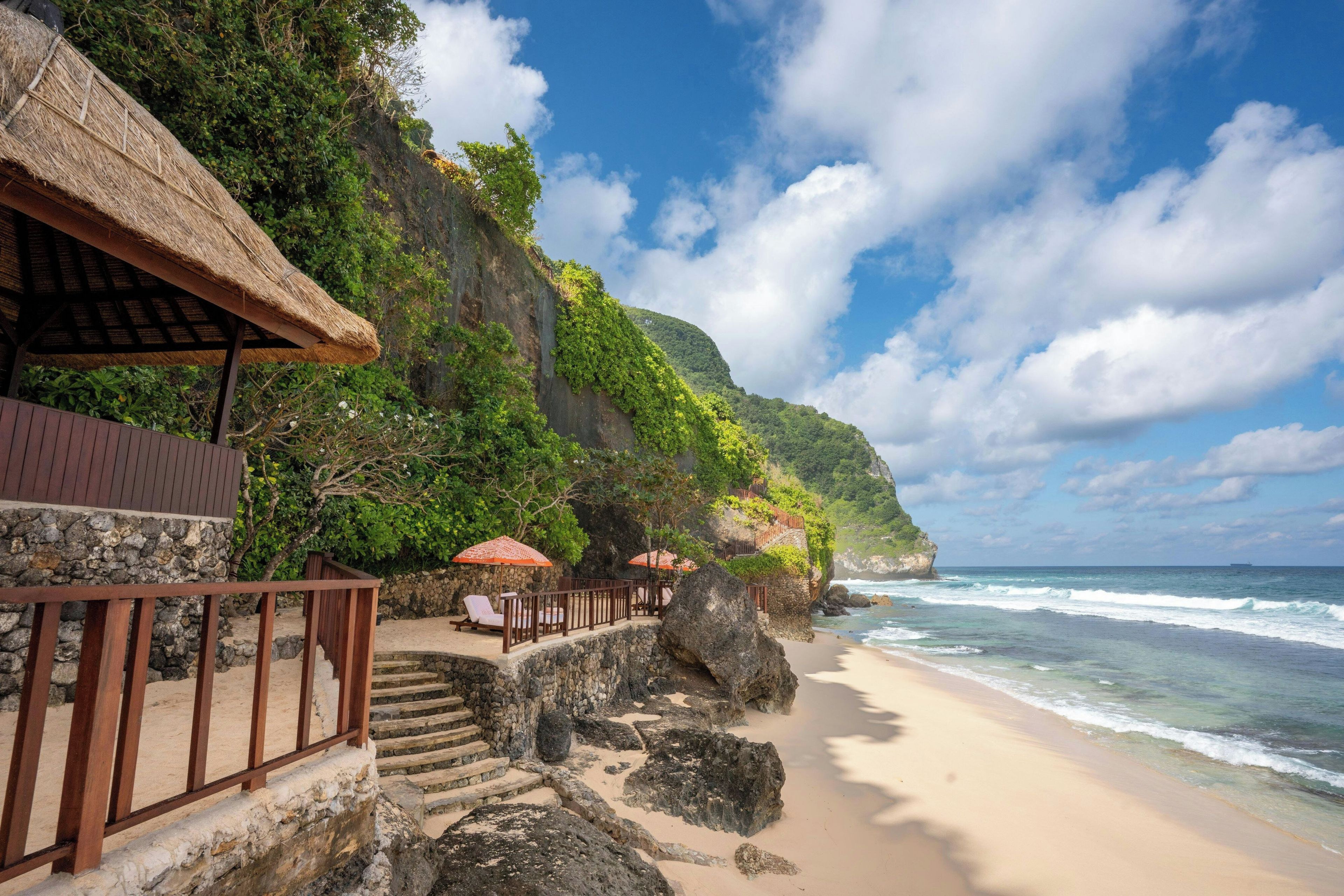 Un resort frente a la playa con una construcción de techo de paja, asientos al aire libre y vista al océano.