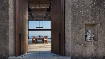 On aperçoit, à travers une grande porte ouverte, un coin repas avec une table et des chaises, un luminaire suspendu et une sculpture en pierre accrochée au mur.