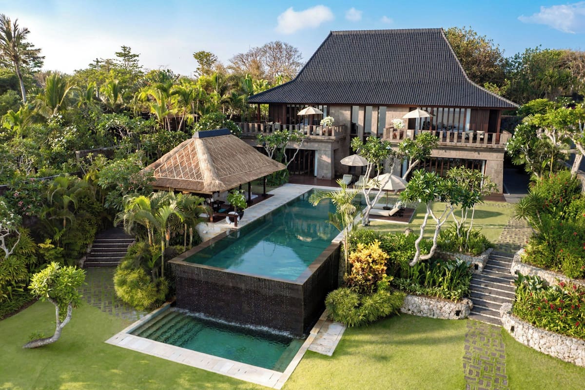 A modern villa with a swimming pool, lush garden, and a traditional thatched roof structure.