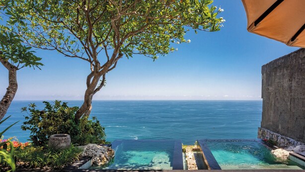 A infinity pool with clear blue water, surrounded by greenery and overlooking the ocean. - Bvlgari Resort Bali (Pecatu)