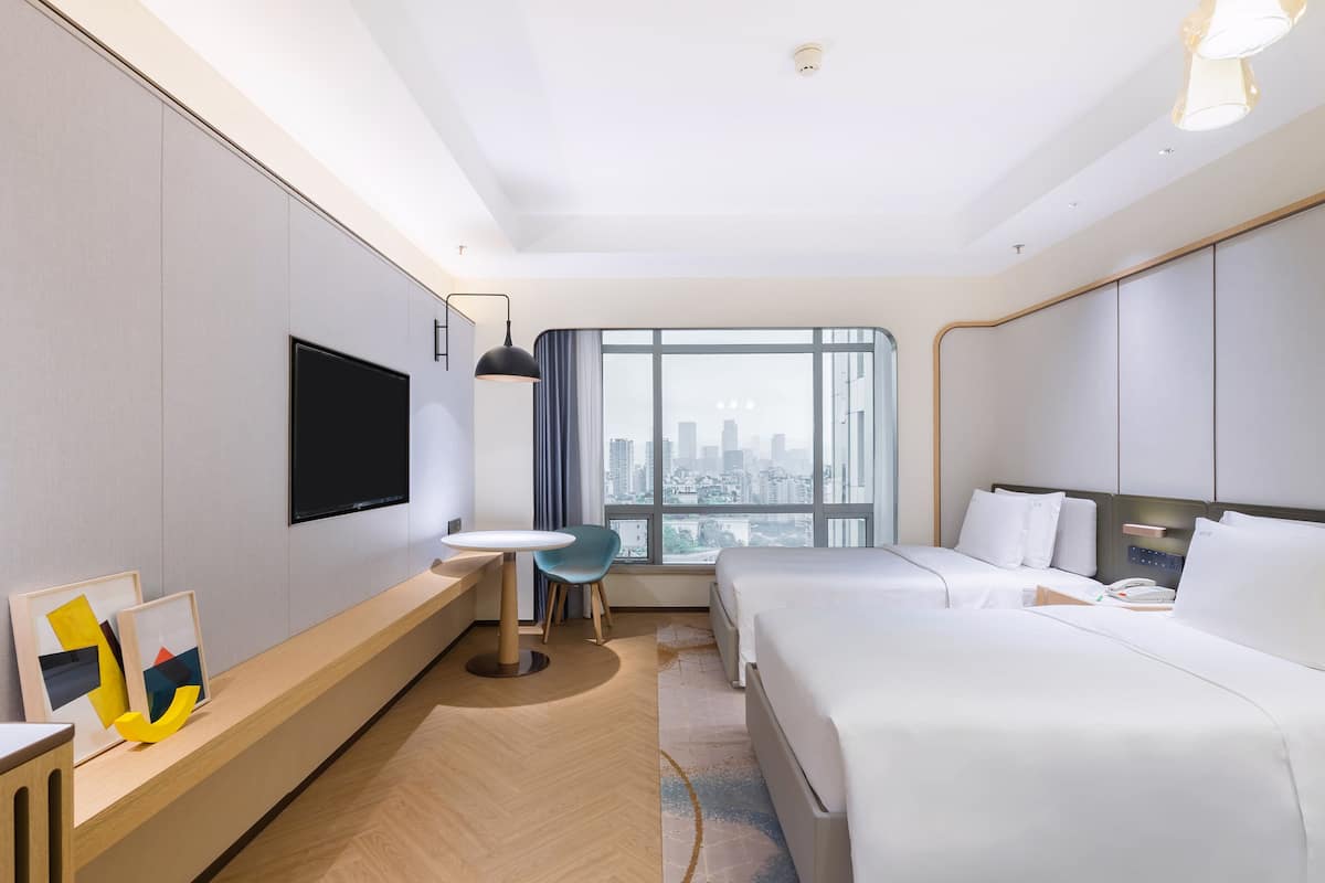Een moderne hotelkamer met een groot bed, een bureau, een stoel, een televisie en een raam met uitzicht op de stad.