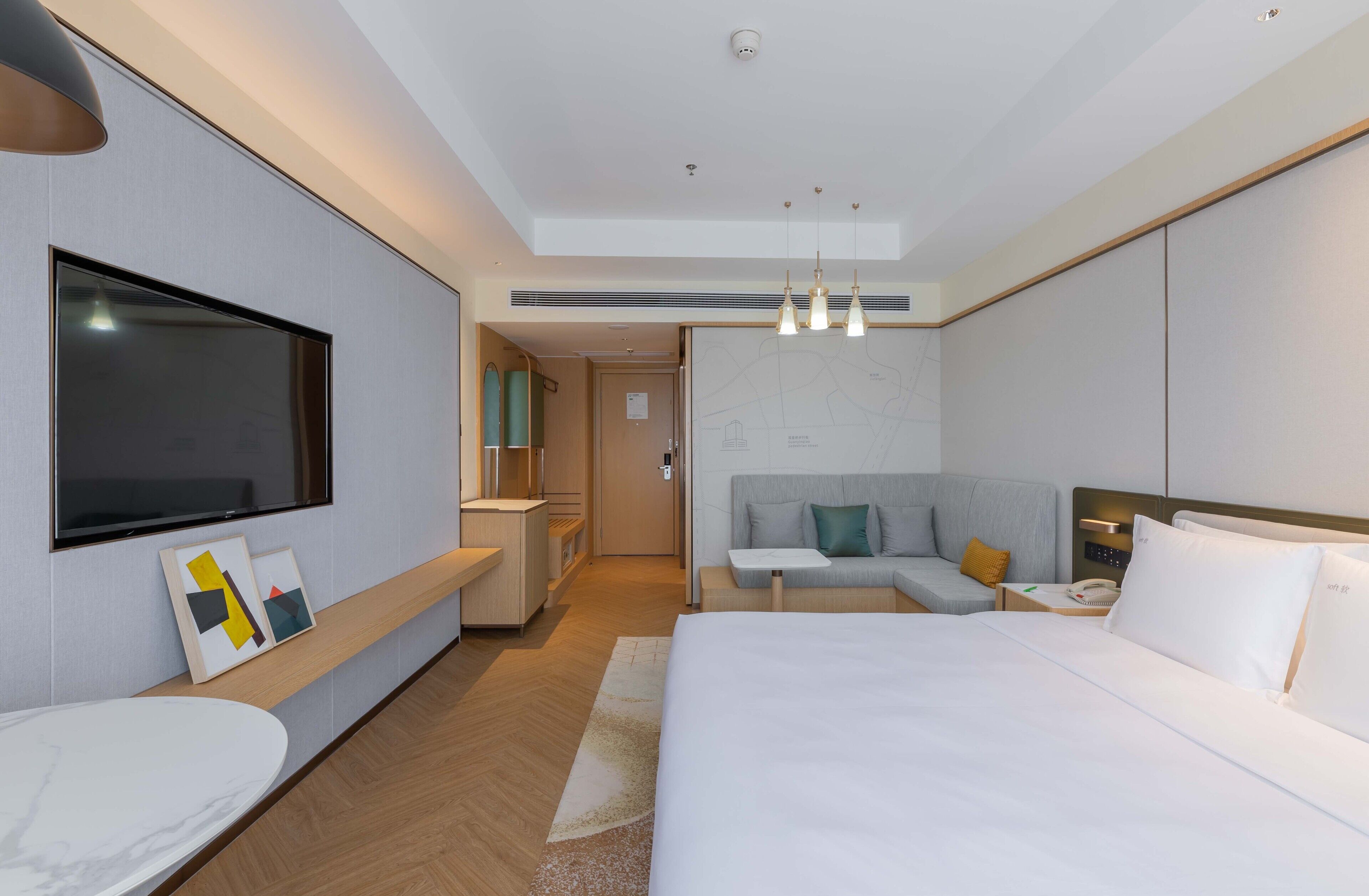 A modern hotel room with a large bed, a desk, a flat-screen TV, and a seating area with a sofa and armchairs.