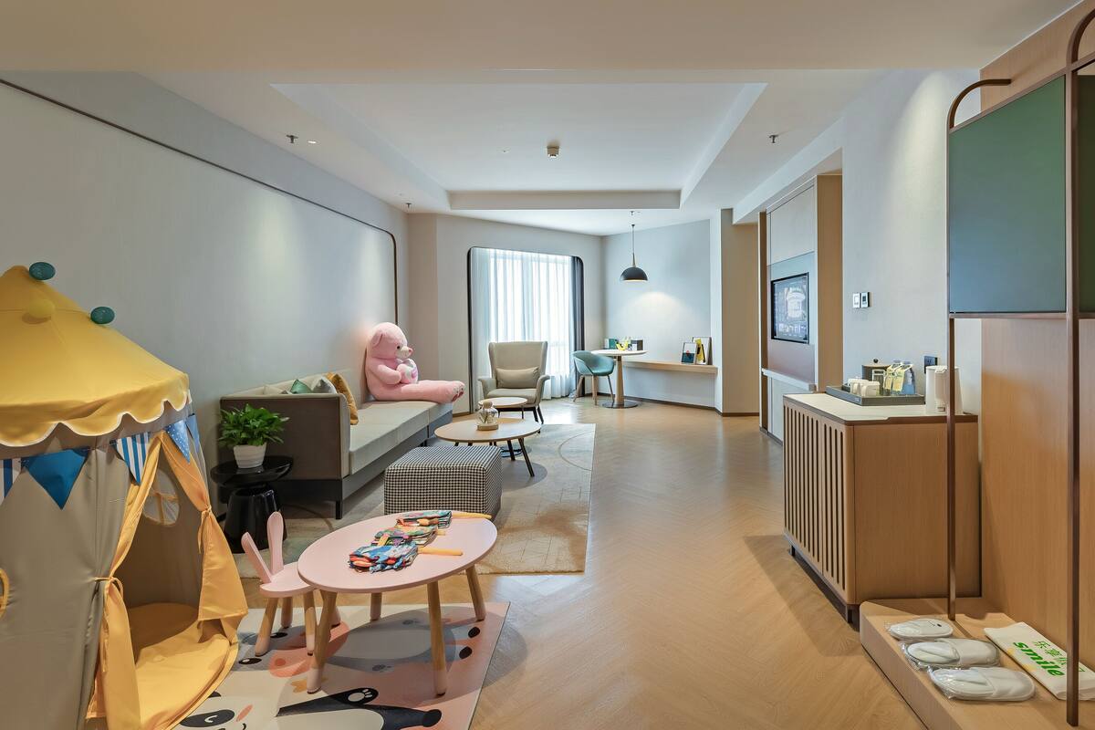 Een moderne woonkamer met een bank, een roze beer, een speelruimte en een keukentoog met spullen erop.