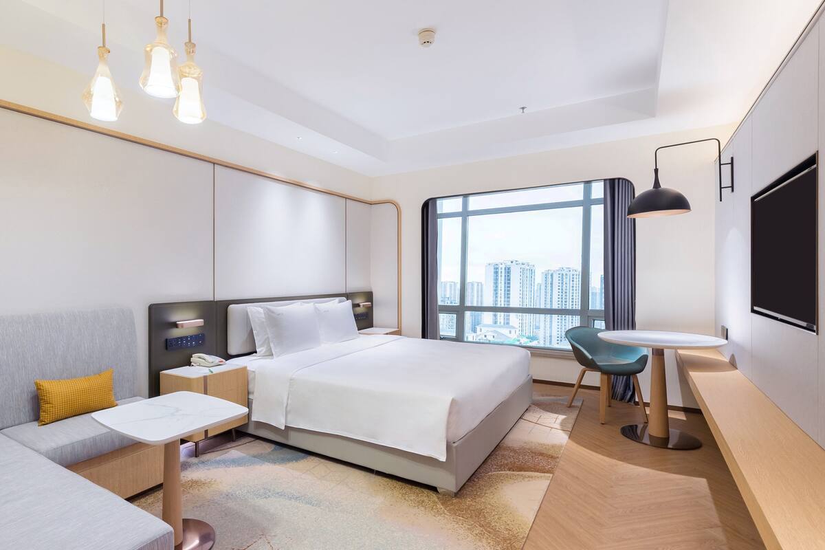 Een moderne hotelkamer met een bed, een bank, een bureau en een groot raam met uitzicht op de stad.