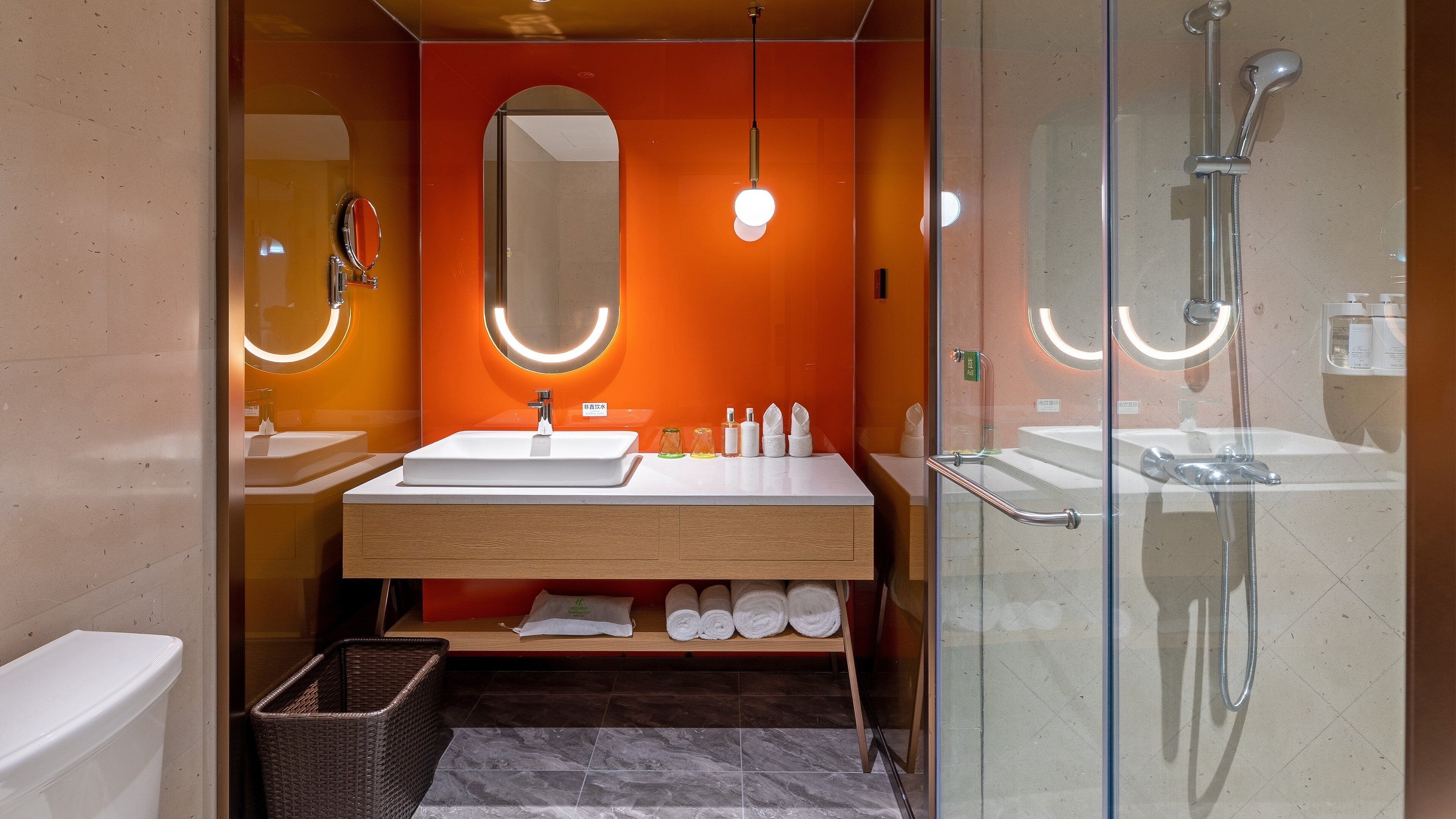 A modern bathroom with a glass-enclosed shower, a white sink, and a mirror with a circular light.
