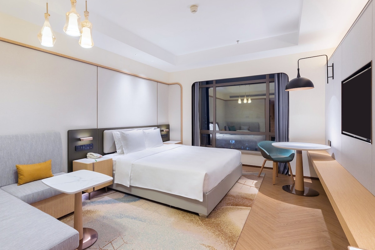 Ett modernt hotellrum med en säng, en soffa, ett litet bord, ett skrivbord och en TV.
