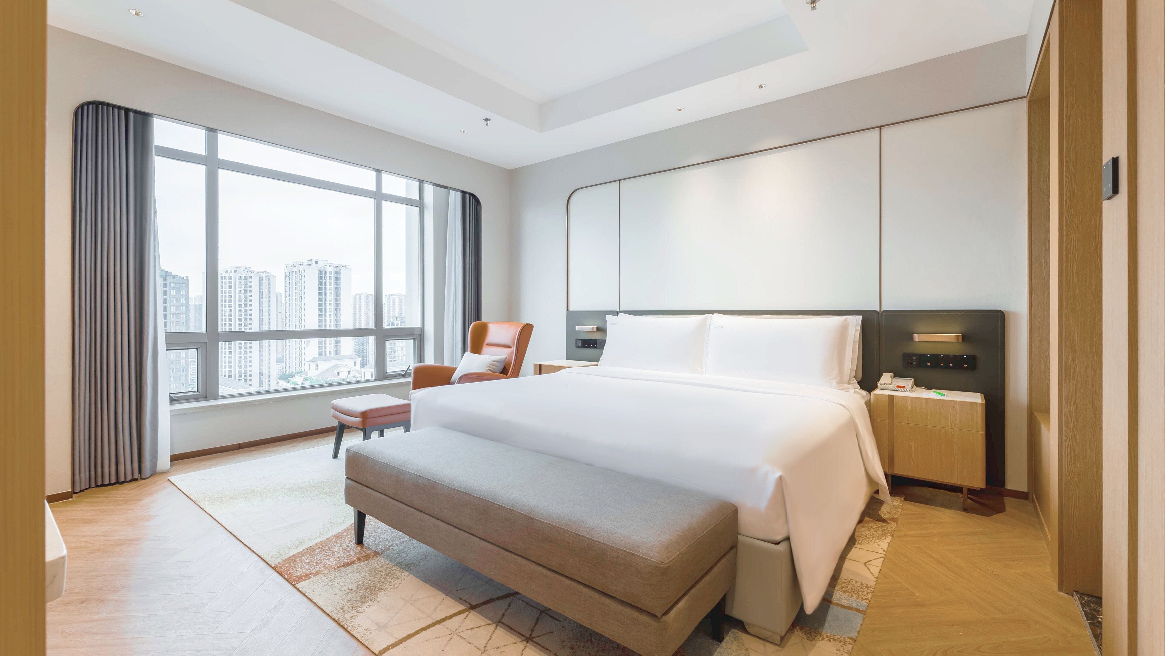 Un hotel moderno con una cama grande, zona de estar, mesita de noche y vistas a la ciudad.