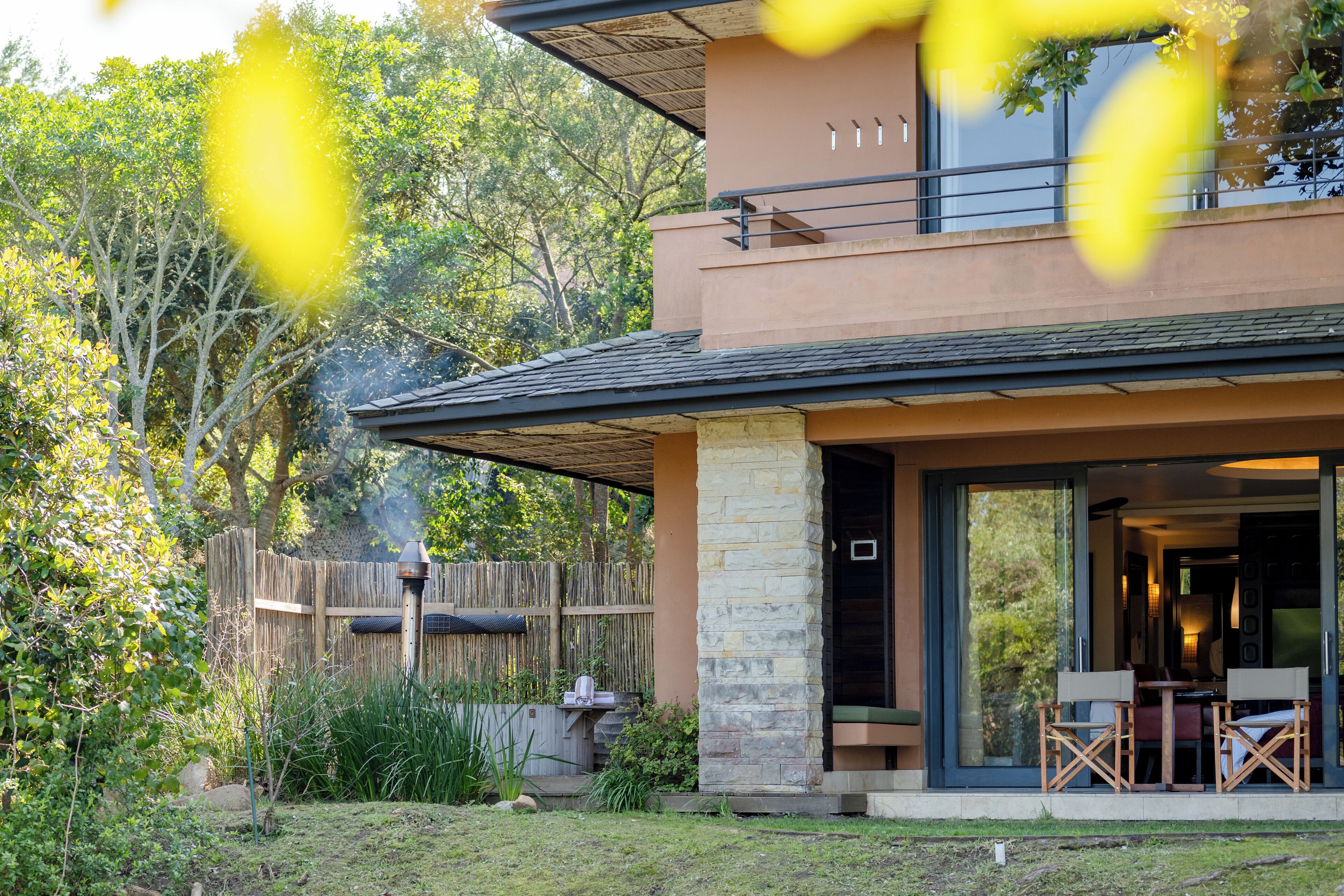 A modern house with a covered patio, stone pillars, and a view of the surrounding greenery.