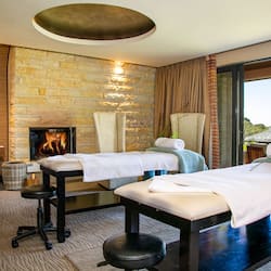 Experience a serene spa retreat with a fireplace, massage tables, and a comfortable chair.