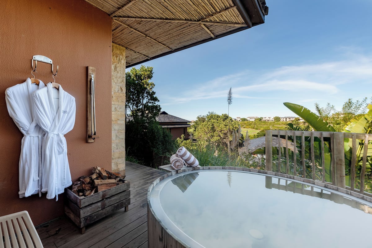 A hot tub on a wooden deck with a view of a house and trees.