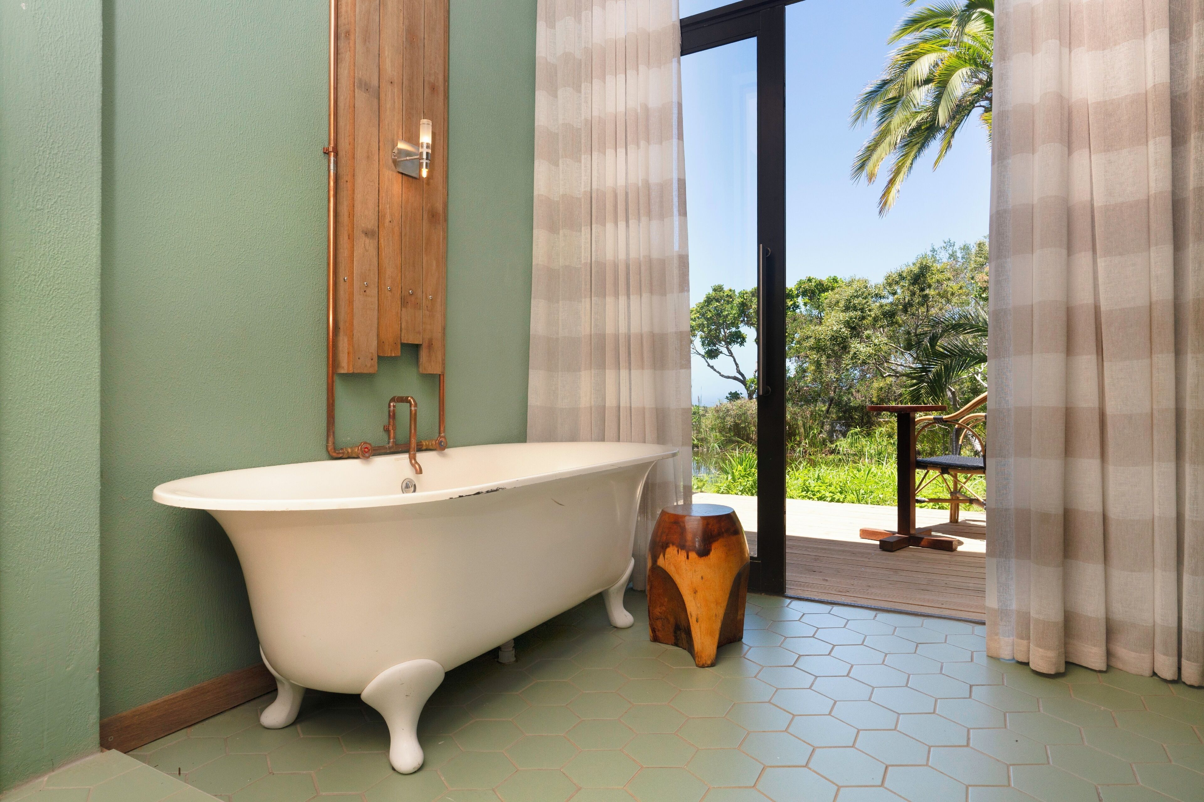 A bathroom with a freestanding bathtub, wooden cabinet, and a view of greenery outside.