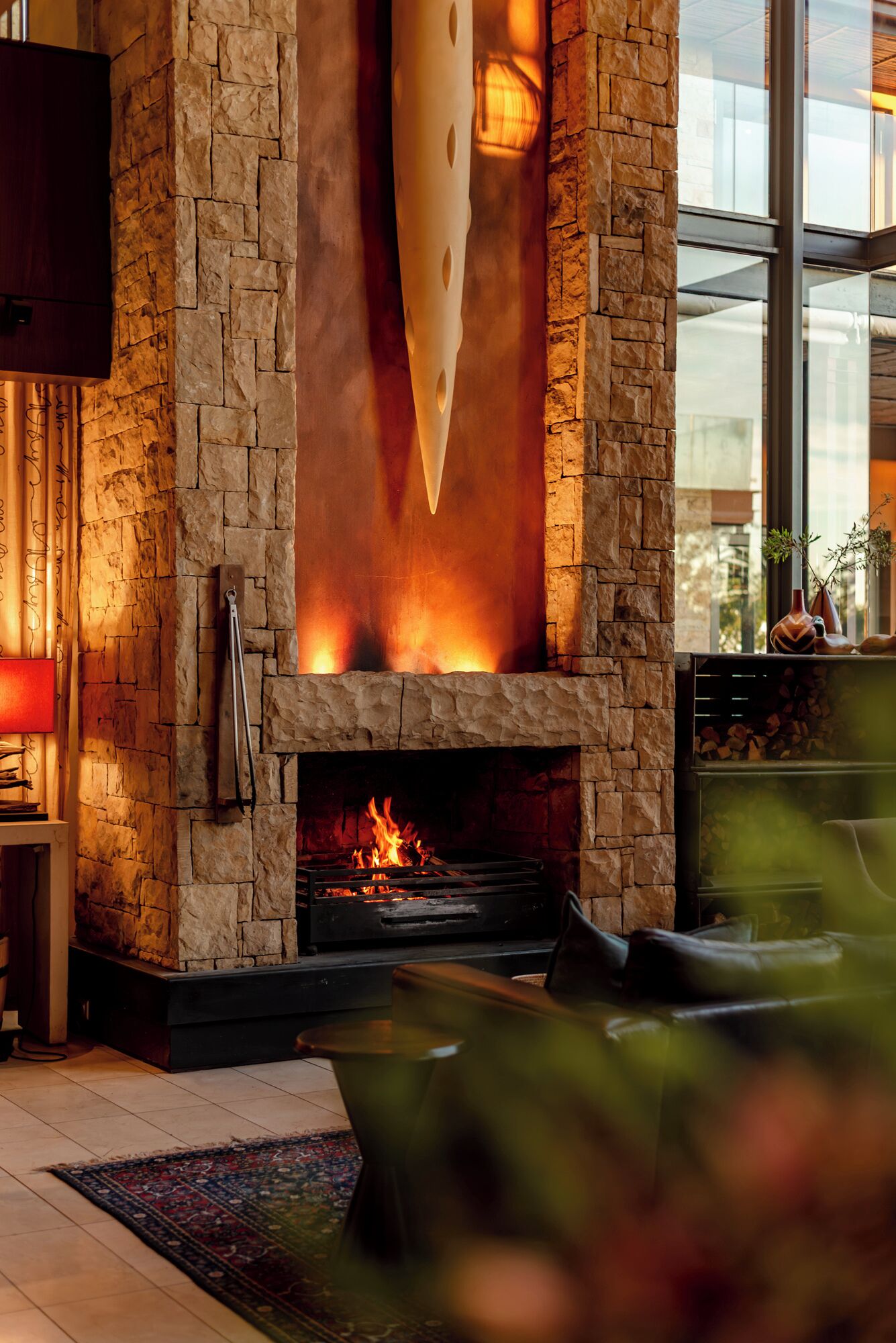 A stone fireplace with a fire, a television mounted on the wall, and a view of the outdoors through a window.
