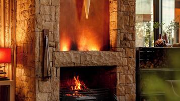 A stone fireplace with a fire, a television mounted on the wall, and a view of the outdoors through a window.