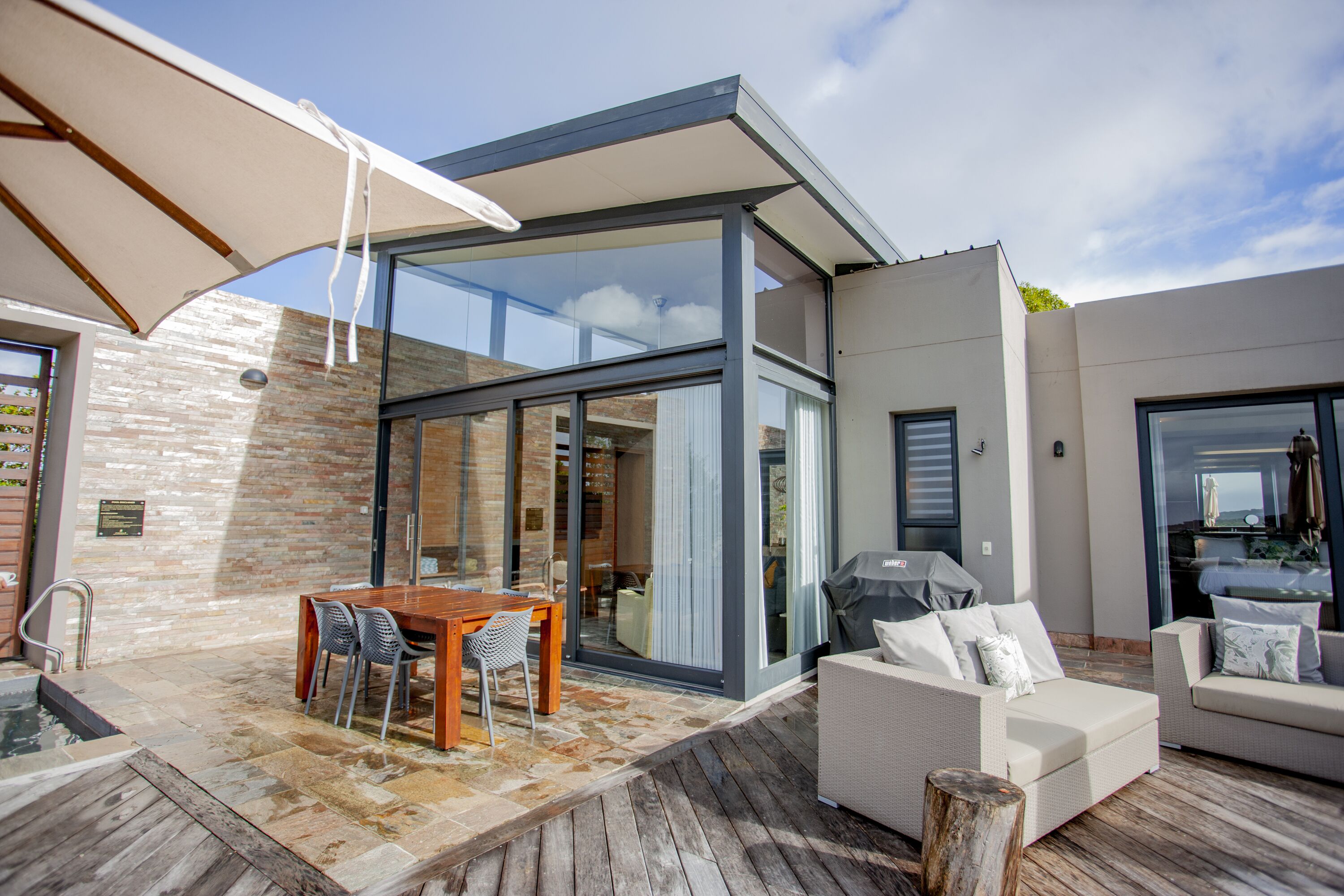 An outdoor patio with a wooden table and chairs, a white sofa, and a grill.