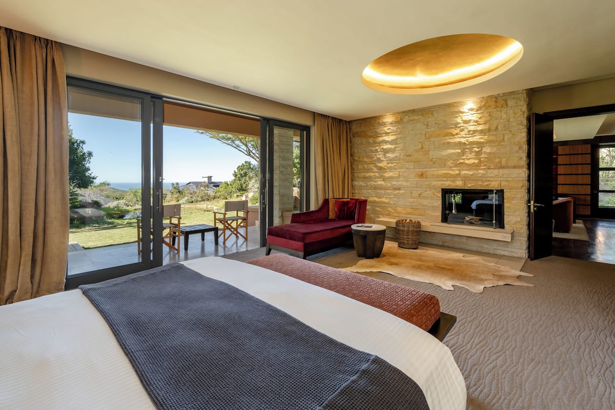 A modern bedroom with a large bed, a fireplace, and a view of the outdoors.