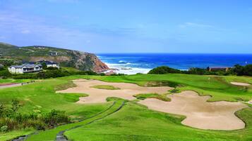 A golf course with bunkers, a flag, and a view of the ocean.