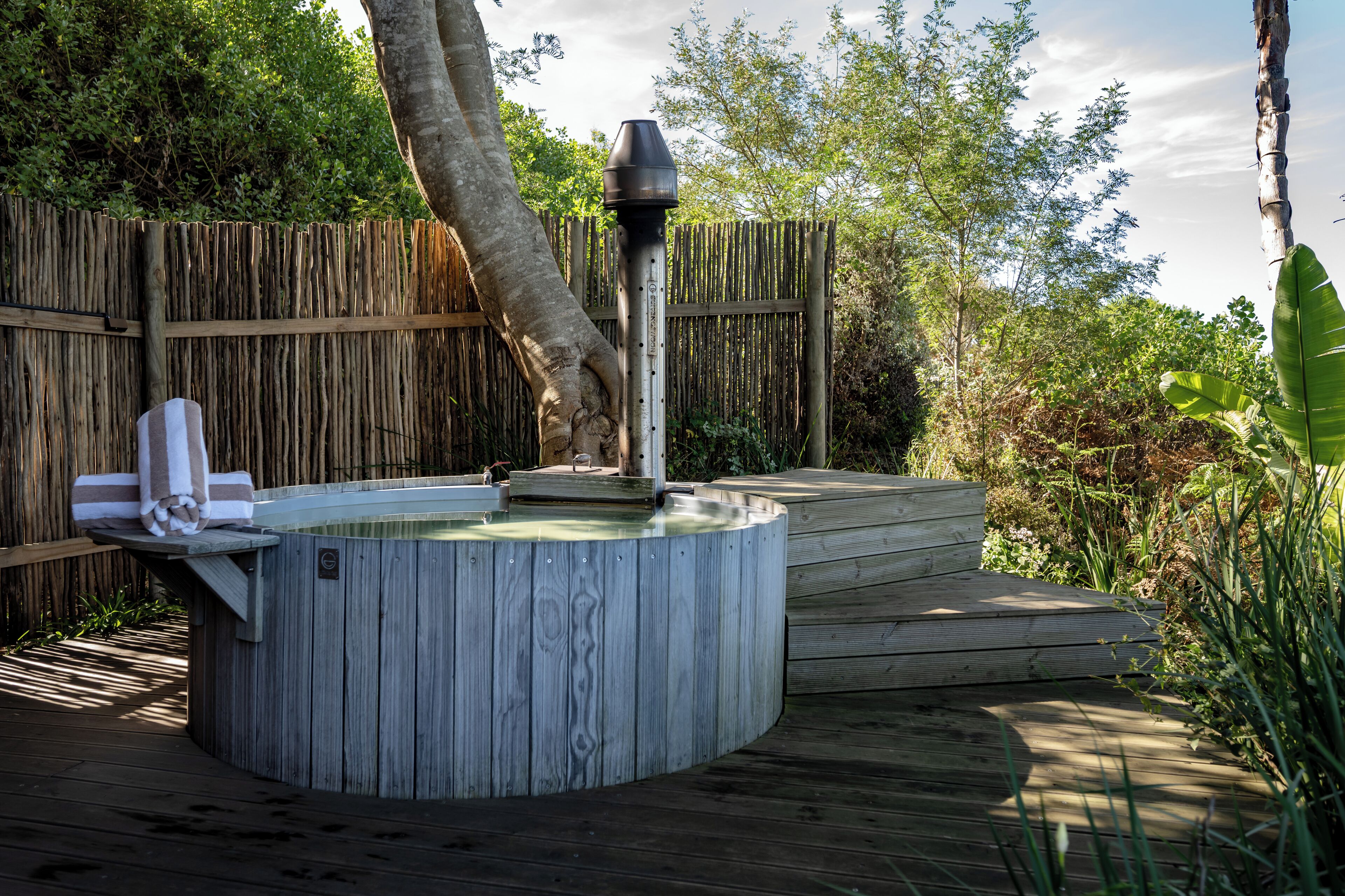 Een houten jacuzzi met een ingebouwde verwarming, omringd door een houten terras en een bamboe omheining.