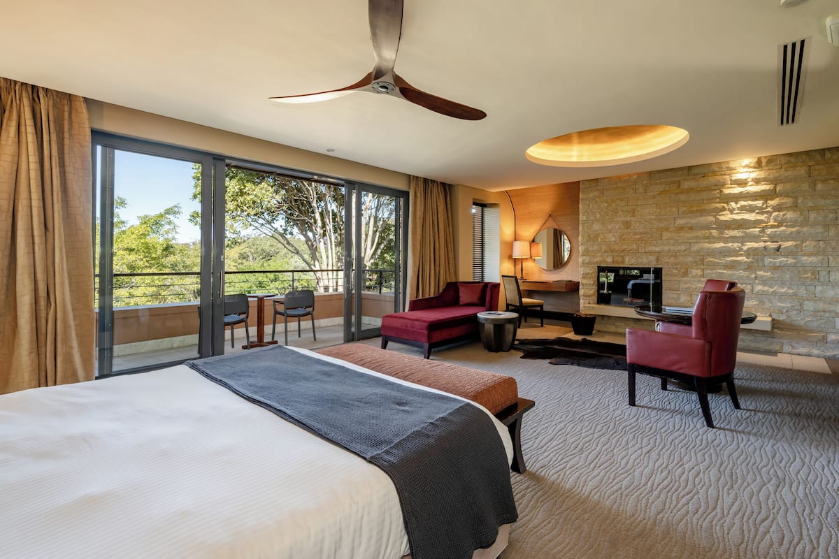 A hotel room with a large bed, a seating area with a sofa and chairs, a television, and a stone fireplace.