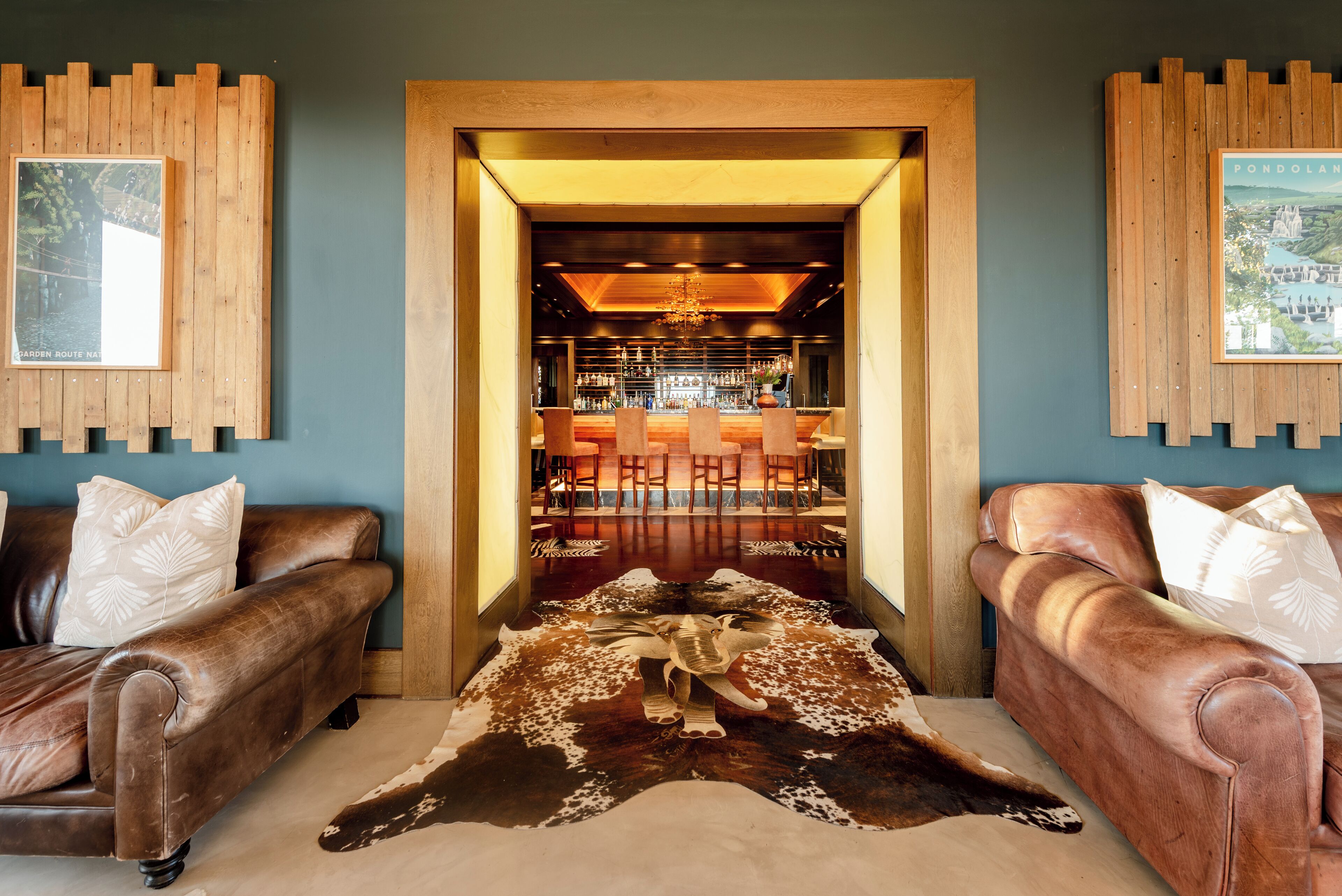 A room with two leather sofas, a wooden coffee table, and a unique cowhide rug with a cow sculpture. A bar area is visible through an open doorway.