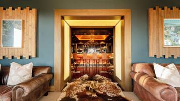 A room with two leather sofas, a wooden coffee table, and a unique cowhide rug with a cow sculpture. A bar area is visible through an open doorway.