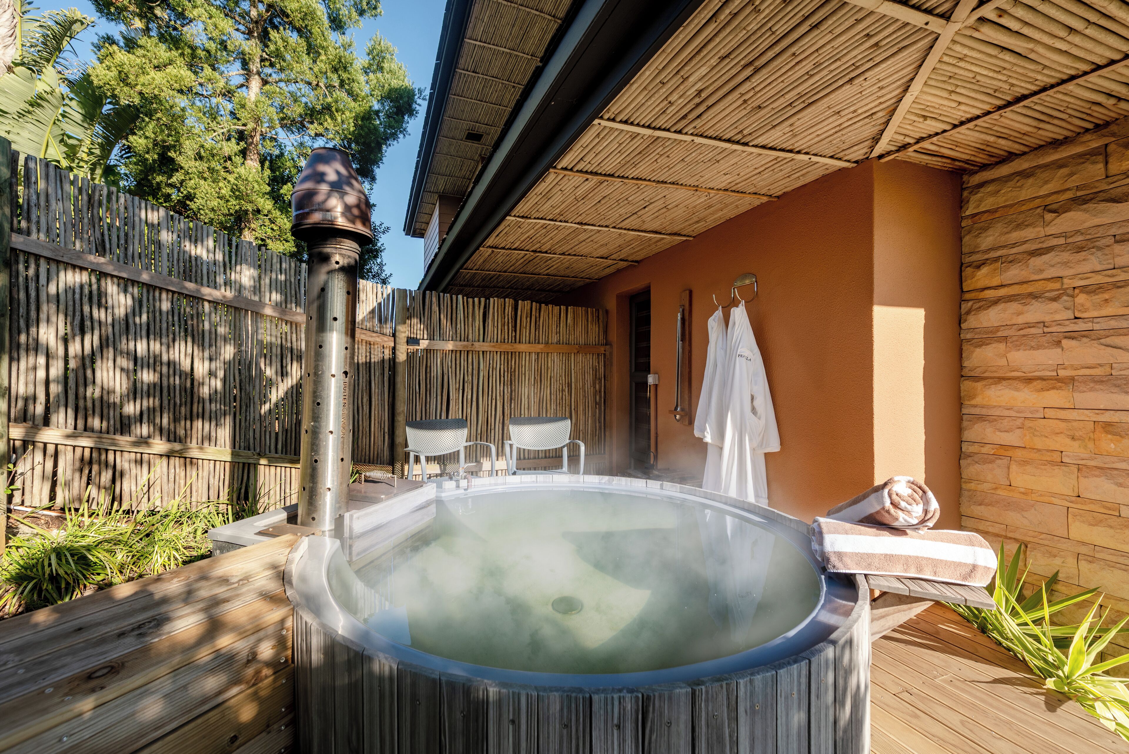 Un jacuzzi con cubierta de madera, techo de bambú y pared de piedra.