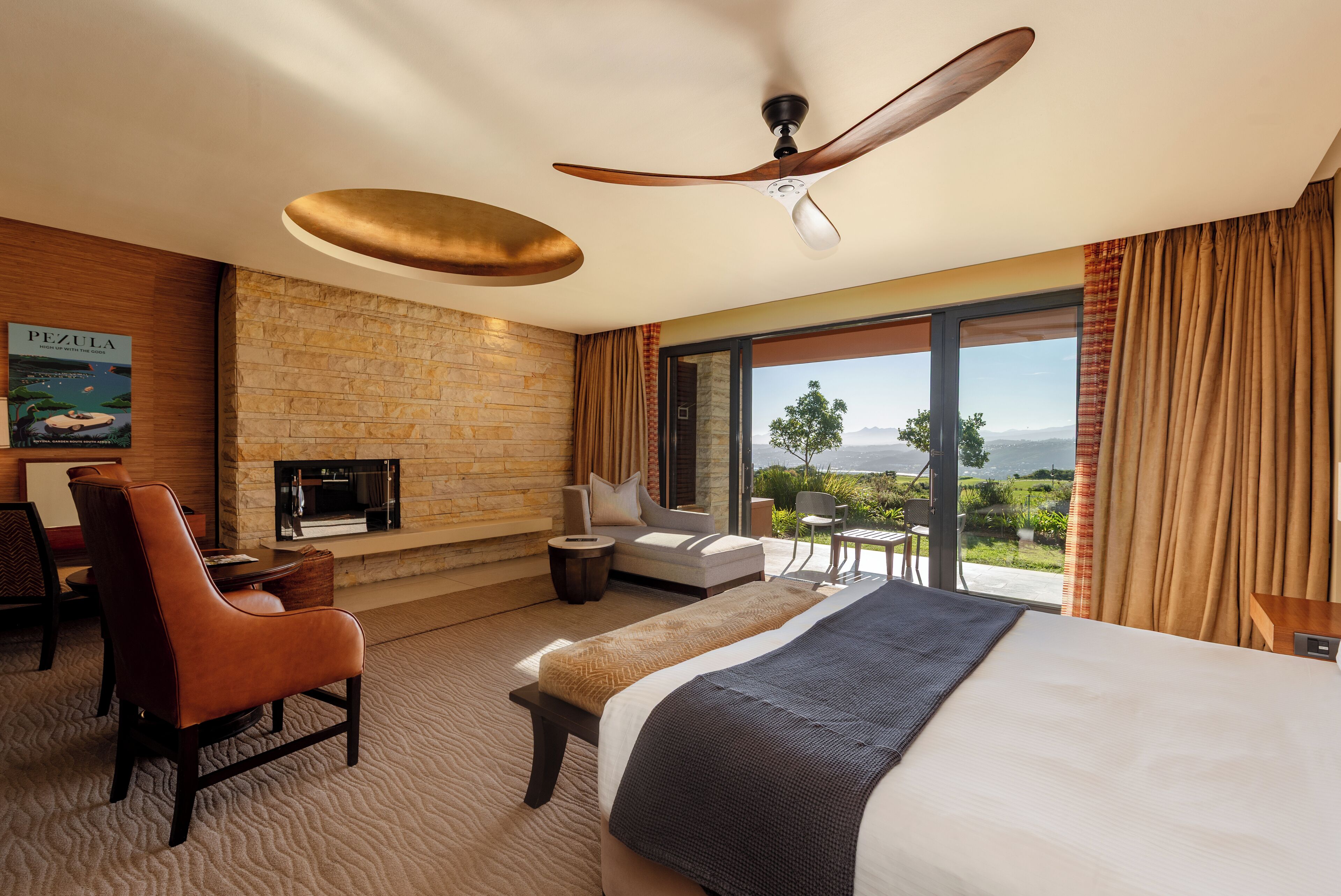 Une chambre d’hôtel avec un mur en pierre, une cheminée, un lit, un canapé, un fauteuil et une vue sur le paysage.
