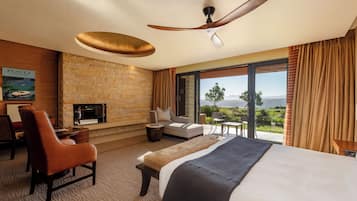 Une chambre d’hôtel avec un mur en pierre, une cheminée, un lit, un canapé, un fauteuil et une vue sur le paysage.