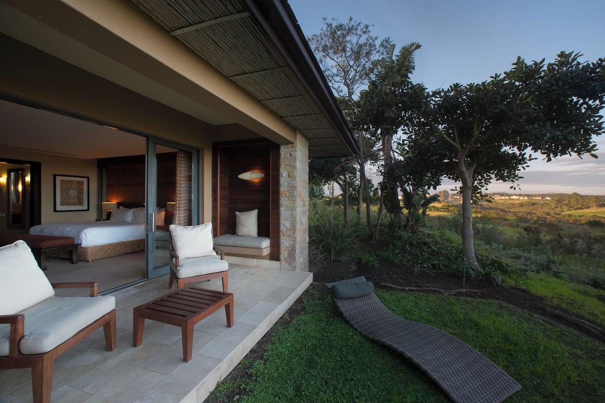 A modern outdoor seating area with a pool, a bedroom with a large bed and a sofa, and a view of the surrounding landscape.