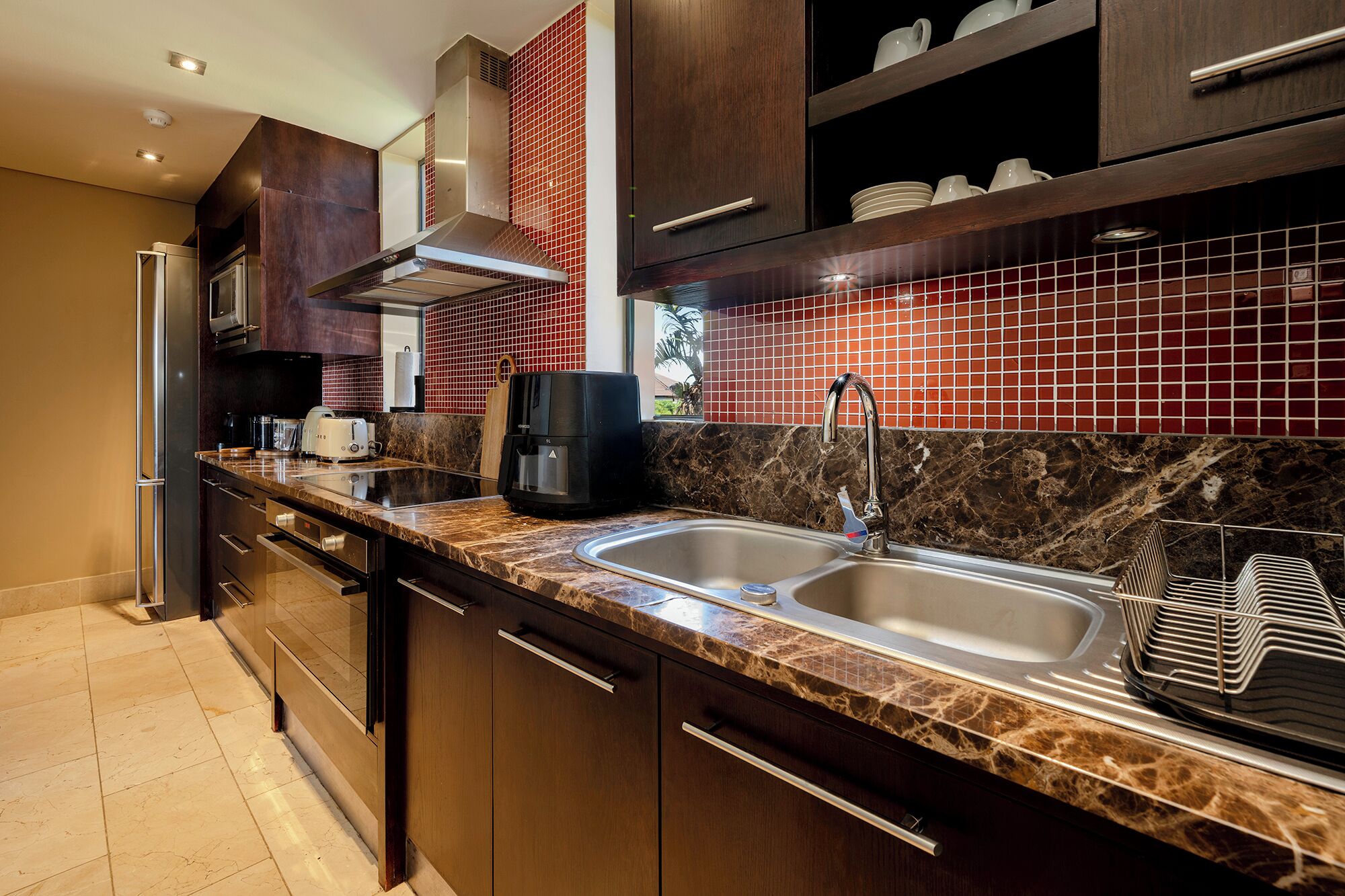 Una cocina moderna con armarios de madera oscura, un lavamanos de acero inoxidable y un salpicadero de azulejos rojos.