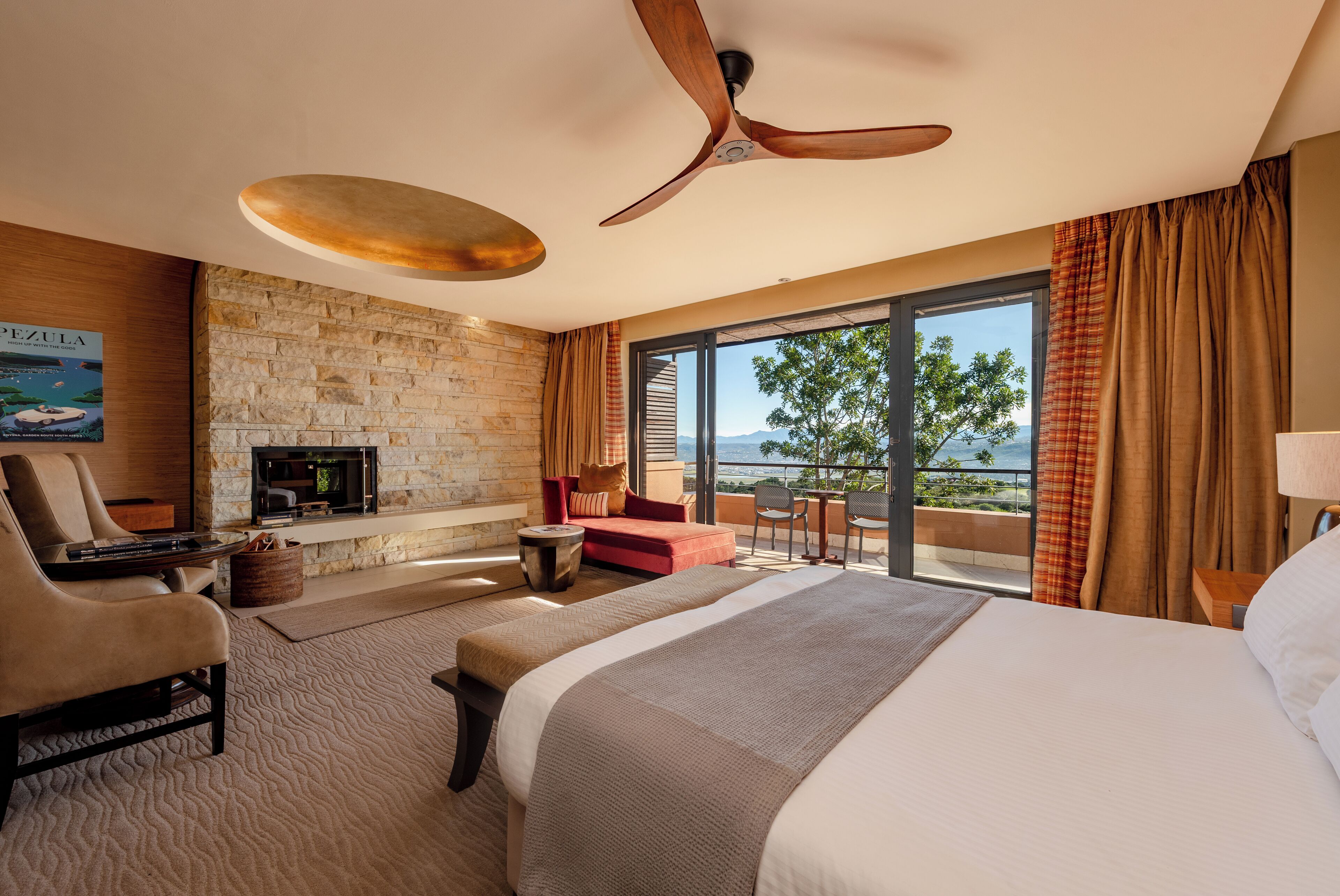 Habitación de hotel con una cama grande, zona de estar con televisor y balcón con vistas.